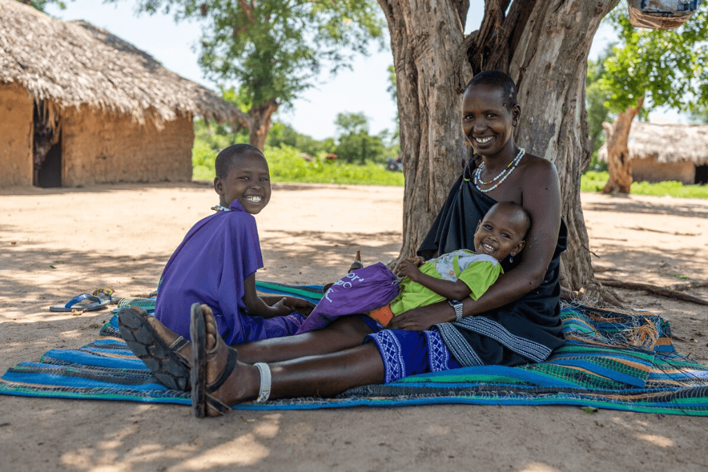 Naning’oi is sitting outside on a mat with her mother, Rose, who is holding her younger sister.