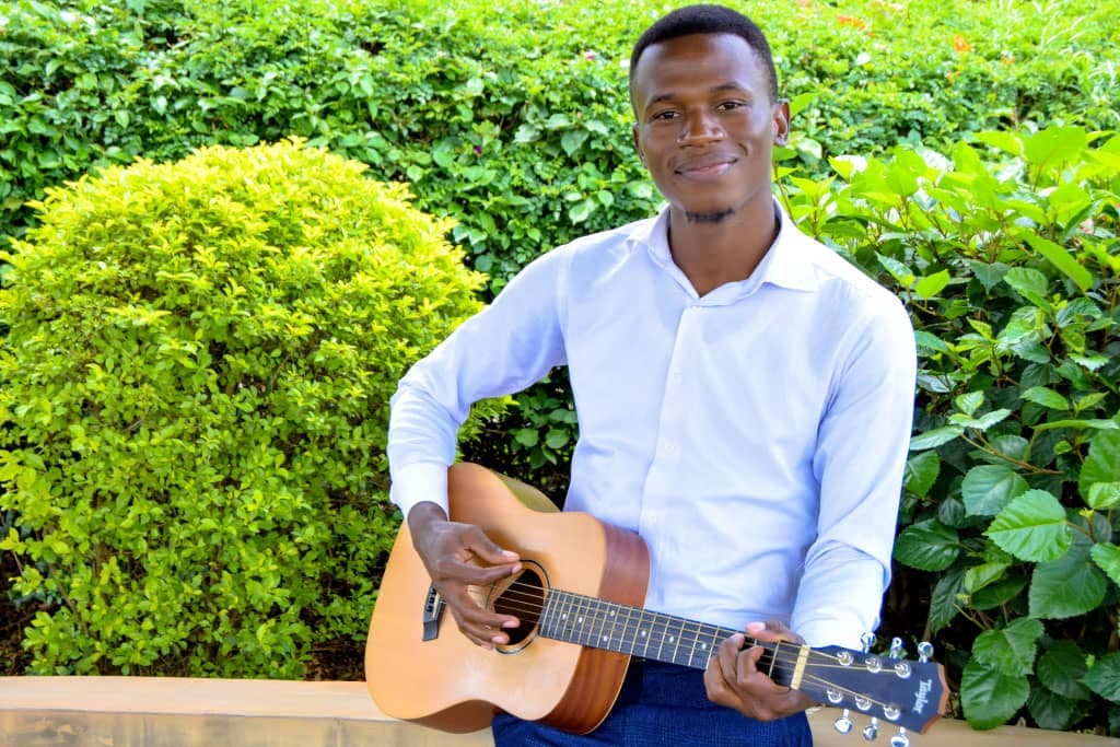 Faida stands outside with his guitar