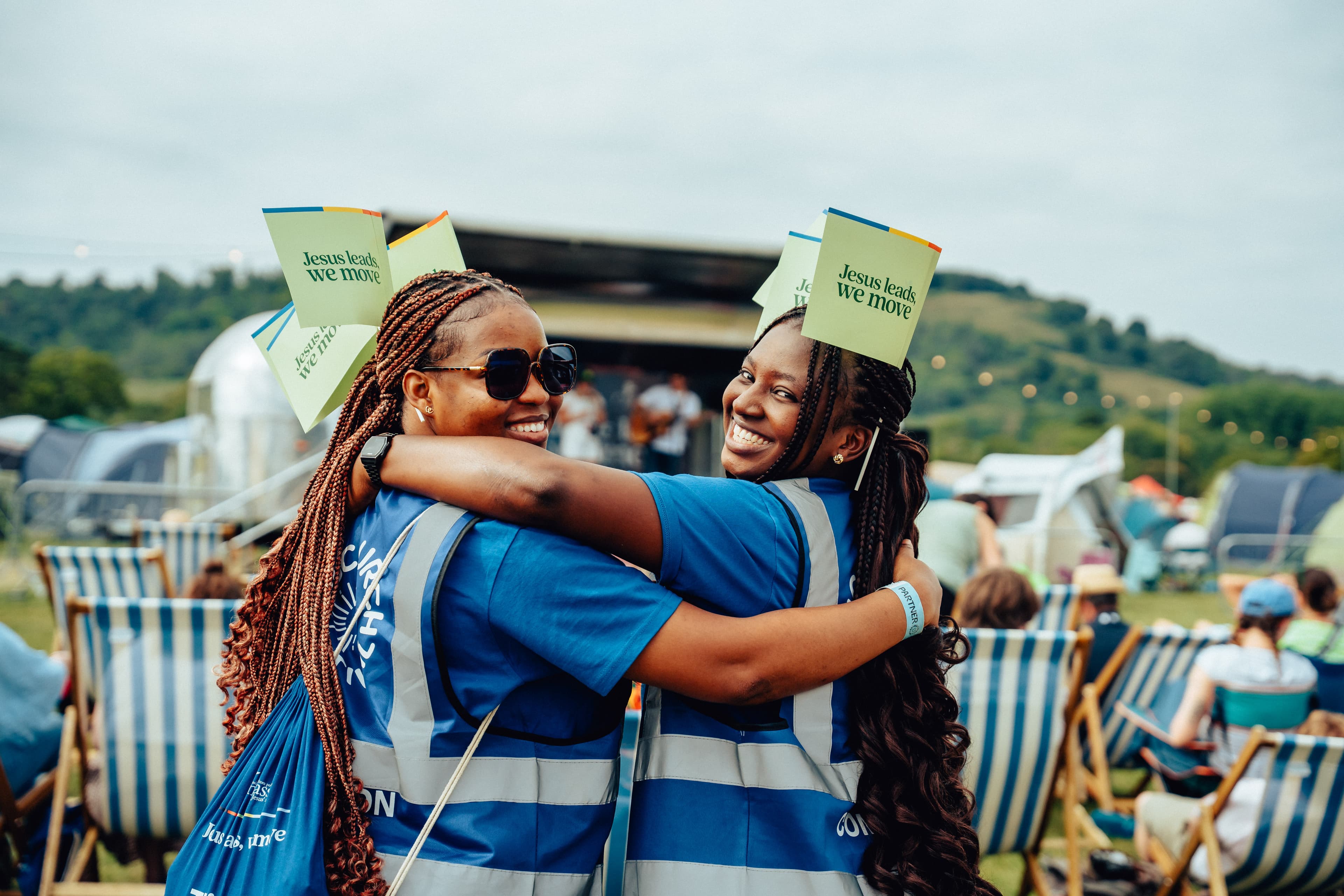 Two girls hugging, smiling, holding 'Jesus leads, we move' flags