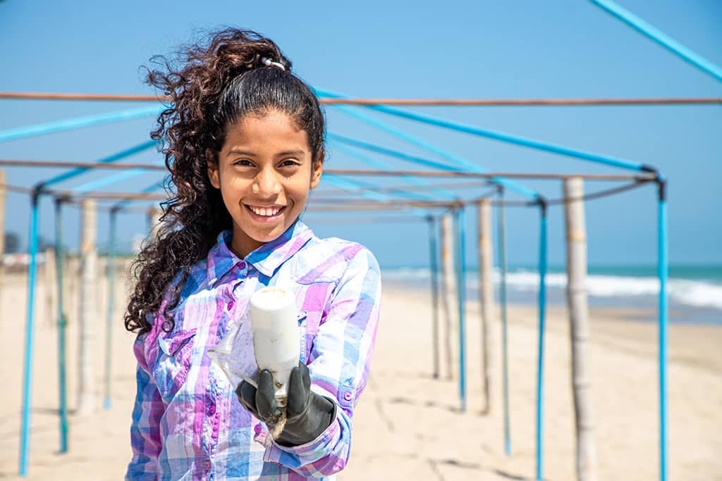 A girl holding out some rubbish collected on a beach
