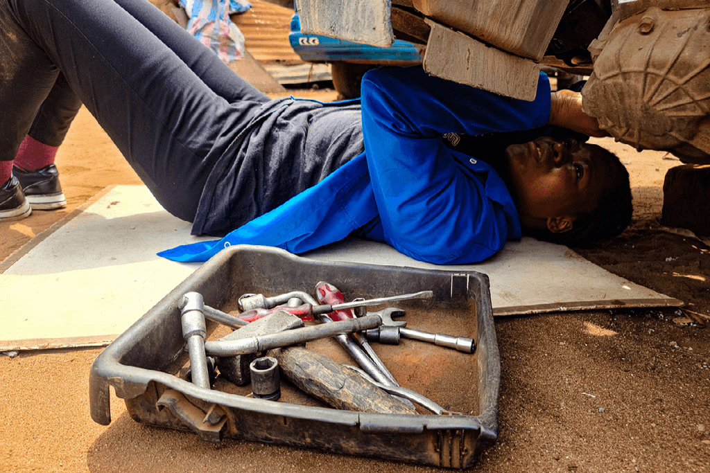Winner works underneath a car with her toolbox beside her.
