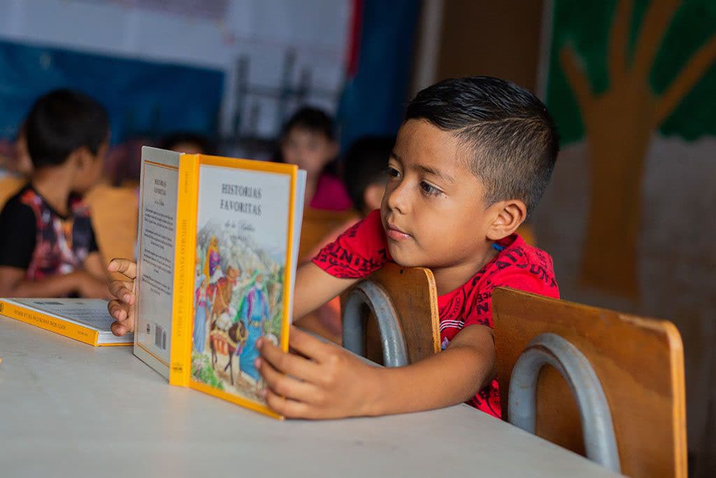 A young boy reading a book in a classroom in Honduras