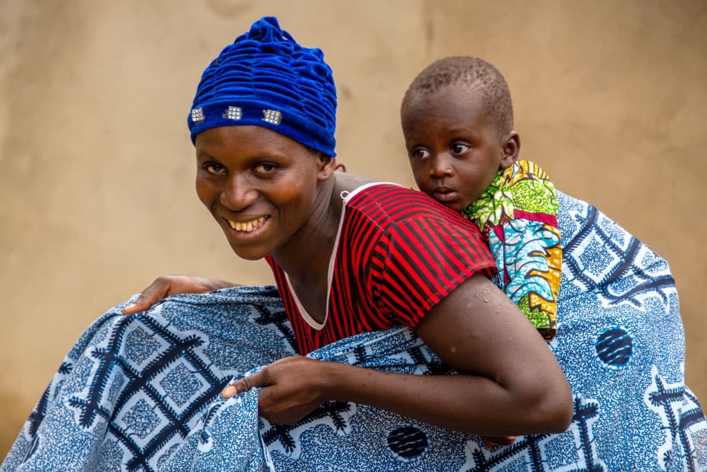 Ama secures a baby on her back using a wrap
