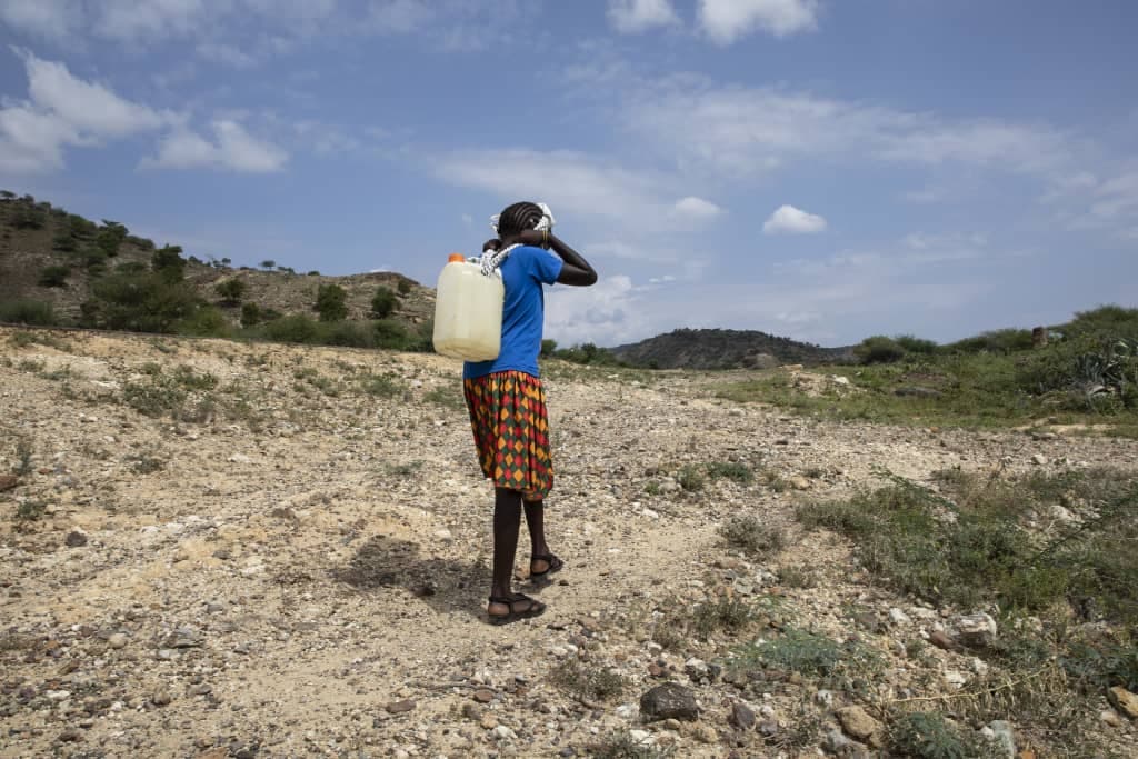 Rehema gathers water in a yellow jerrycan
