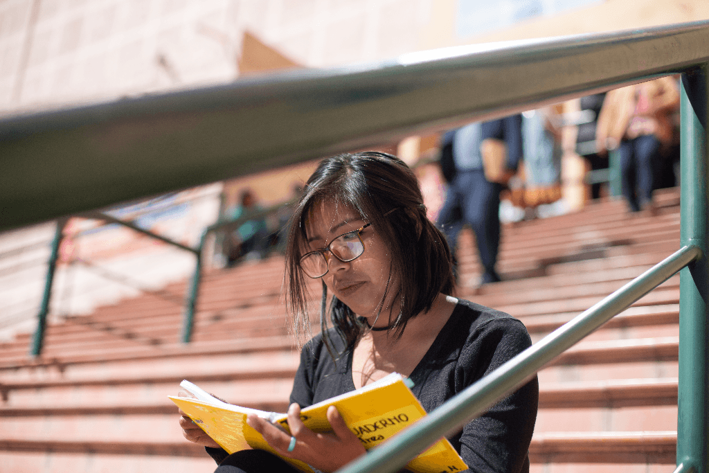 Lidia is sitting on a staircase and holding a yellow notebook.
