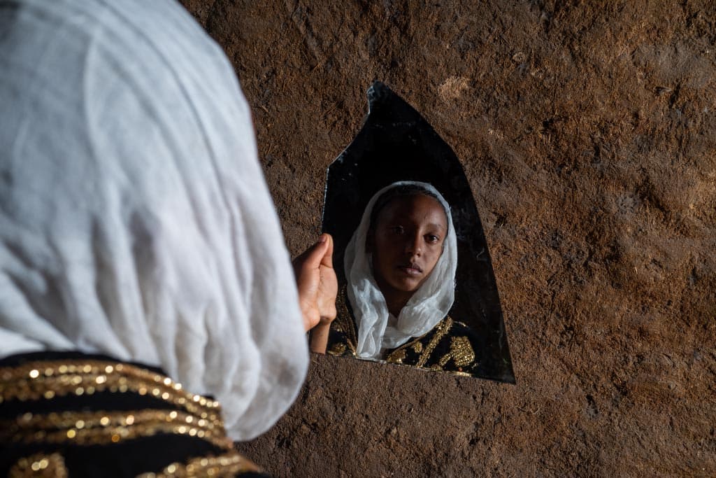 Mart, in bridal dress, looks into a broken mirror.