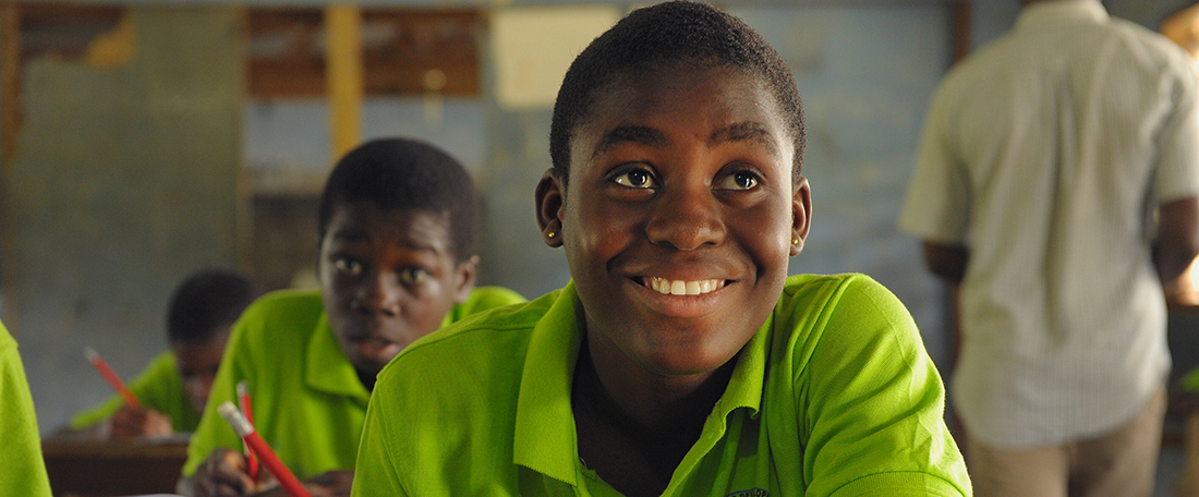 Ghanan students in classroom, wearing bright green uniforms and sitting at wood desks.