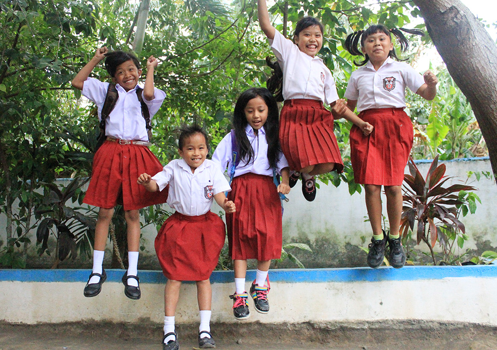 Bintang and her friends wearing their school uniforms and jumping off a low wall. 