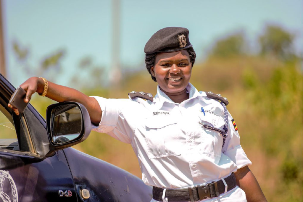 Doreen is leaning on a police vehicle, wearing her white police uniform and smiling.