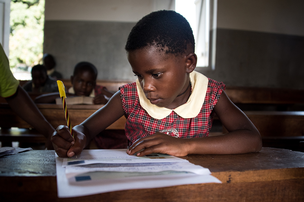 A girl in a classroom in Uganda writing a letter