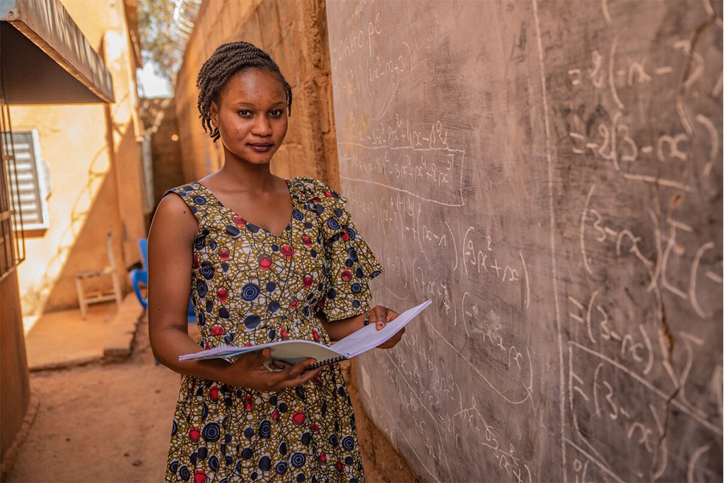Fatoumata stood next to a blackboard, holding her textbook. 