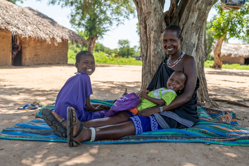 Naning’oi is sitting outside on a mat with her mother, Rose, who is holding her younger sister.