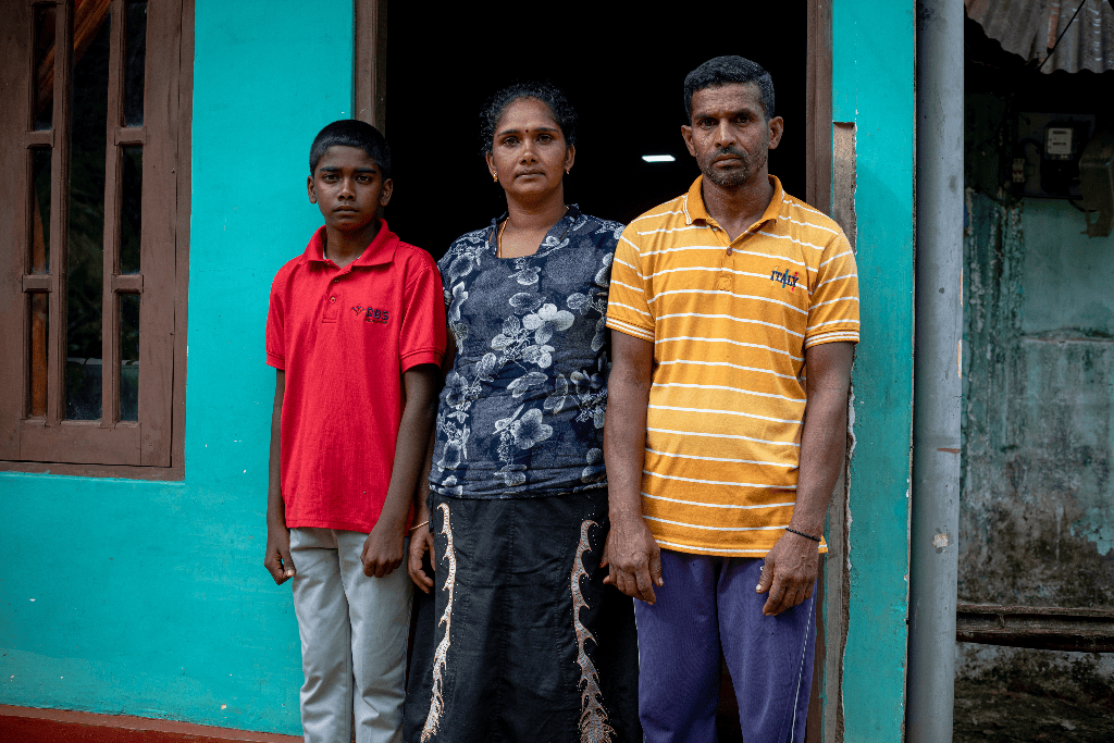 Akshan is standing in front of his home with his mother and father.