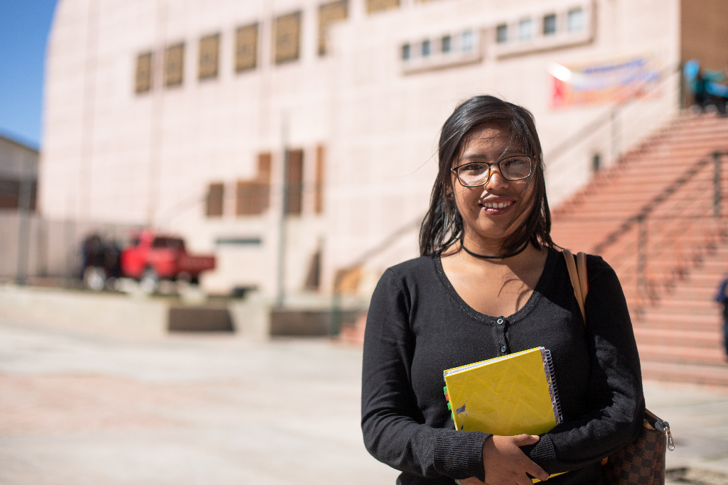 Lidia is holding a yellow notebook standing outside the building.