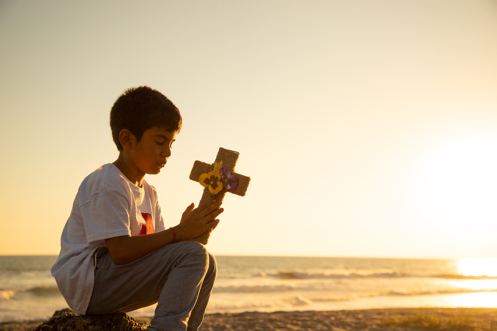 Josue is sitting on a rock at a beach in El Salvador and is holding a cross.